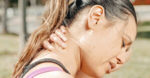 Young woman clutching back of neck and grimacing due to neck pain